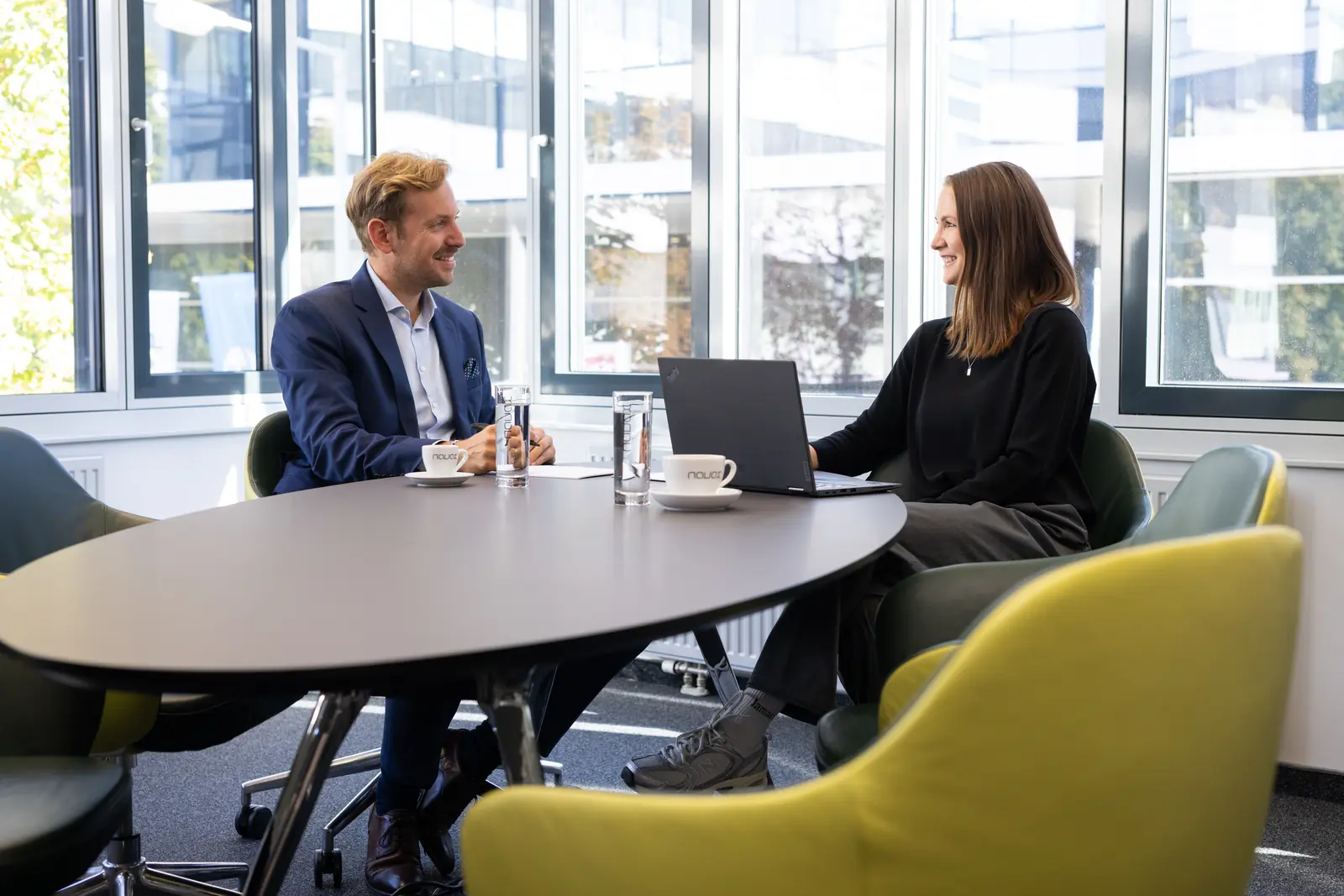 Ein Mann und eine Frau im Gespräch an einem Besprechungstisch mit Laptop