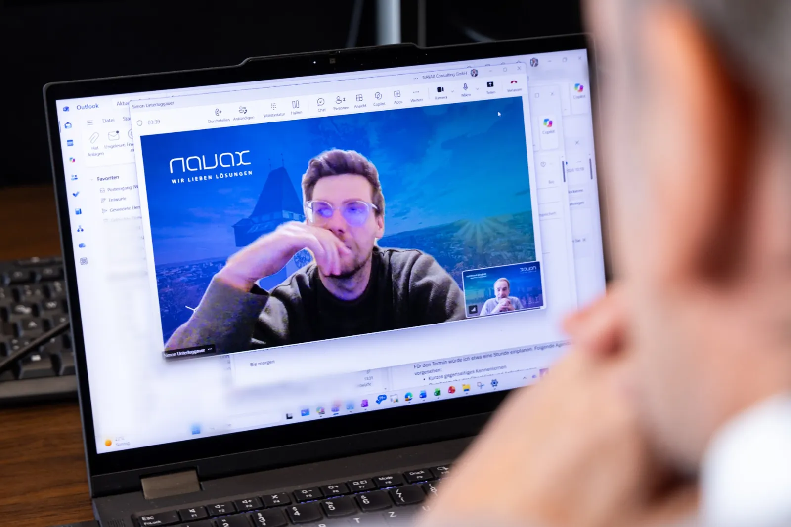Videocall auf einem Laptop, im Vordergrund die Schulter einer Person