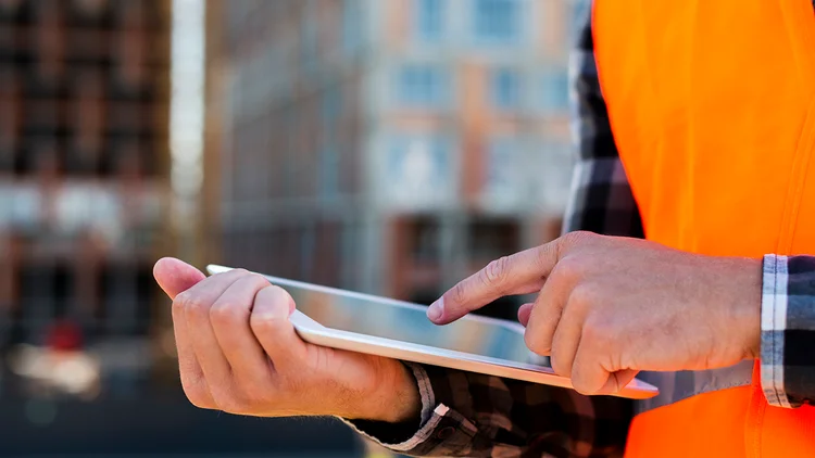 Mann auf Baustelle hält Laptop in der Hand und analysiert die Liquidität 