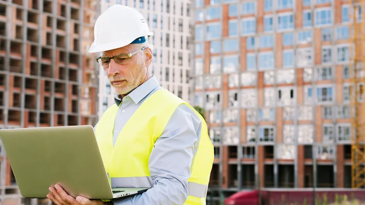 Mann hält Laptop in der Hand und arbeitet auf Baustelle 