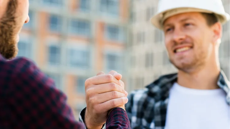Zwei junge Männer lächeln sich an und klatschen auf Baustelle ein