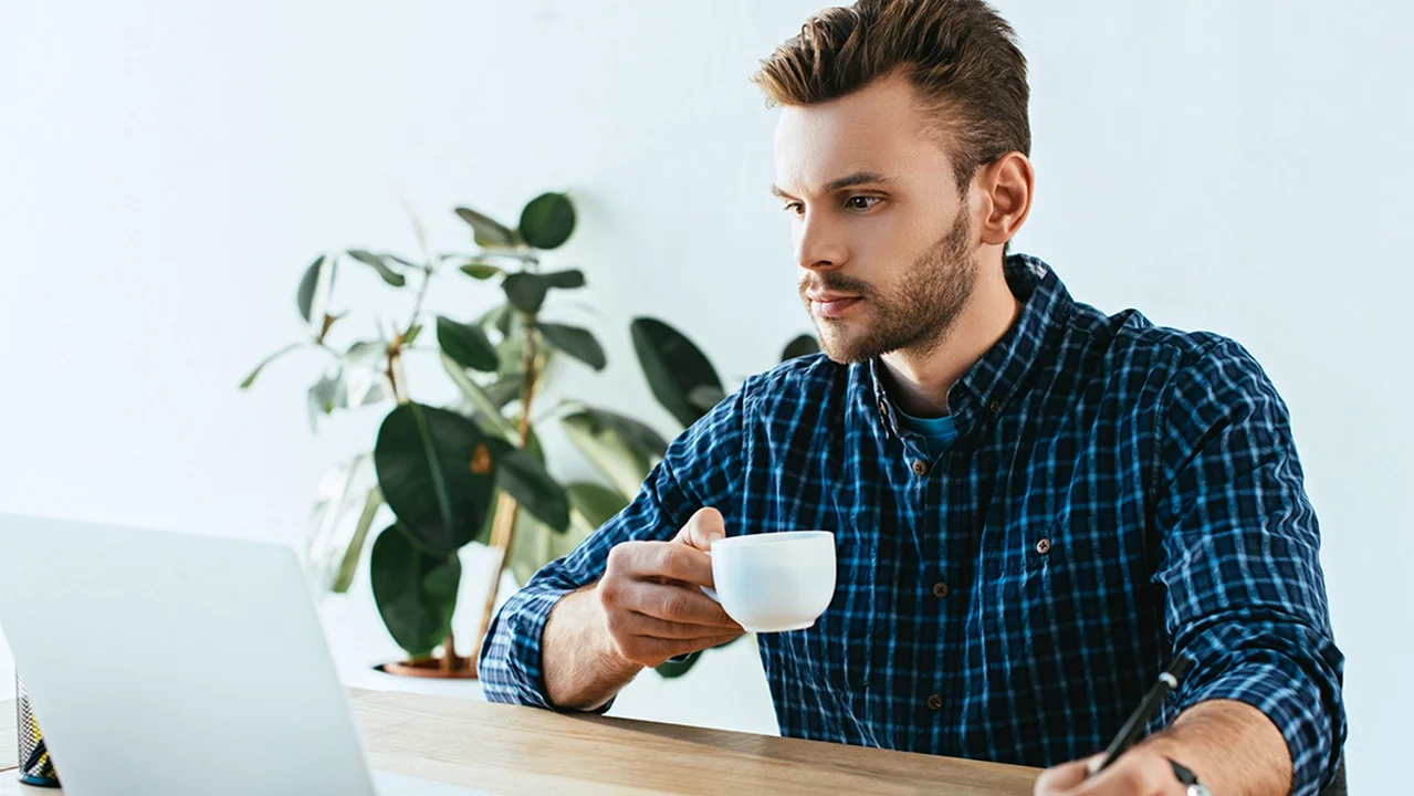 Mann schaut auf Bildschirm mit Kaffeetasse
