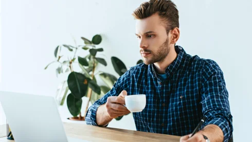 Mann schaut auf Laptop mit Kaffee