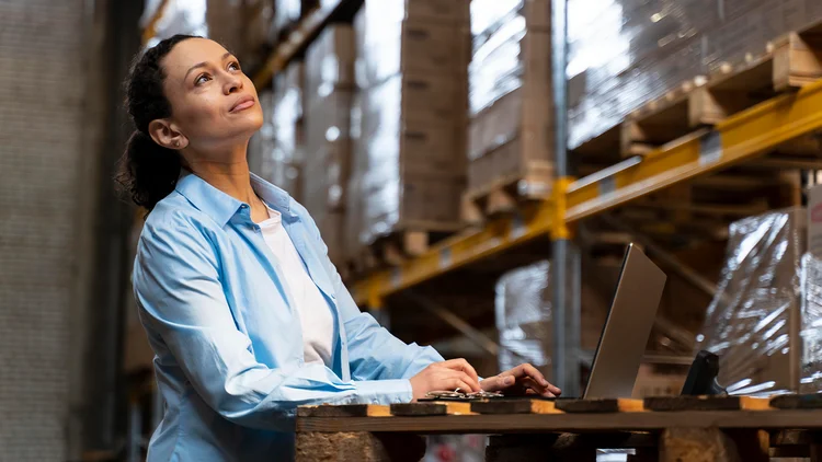 Frau lächelt im Lager und arbeitet am Computer