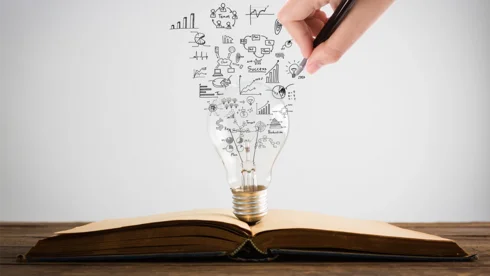 Ein aufgeschlagenes Buch mit einer Glühbirne aus Business Intelligence Symbolen