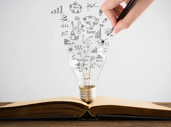 Ein aufgeschlagenes Buch mit einer Glühbirne aus Business Intelligence Symbolen