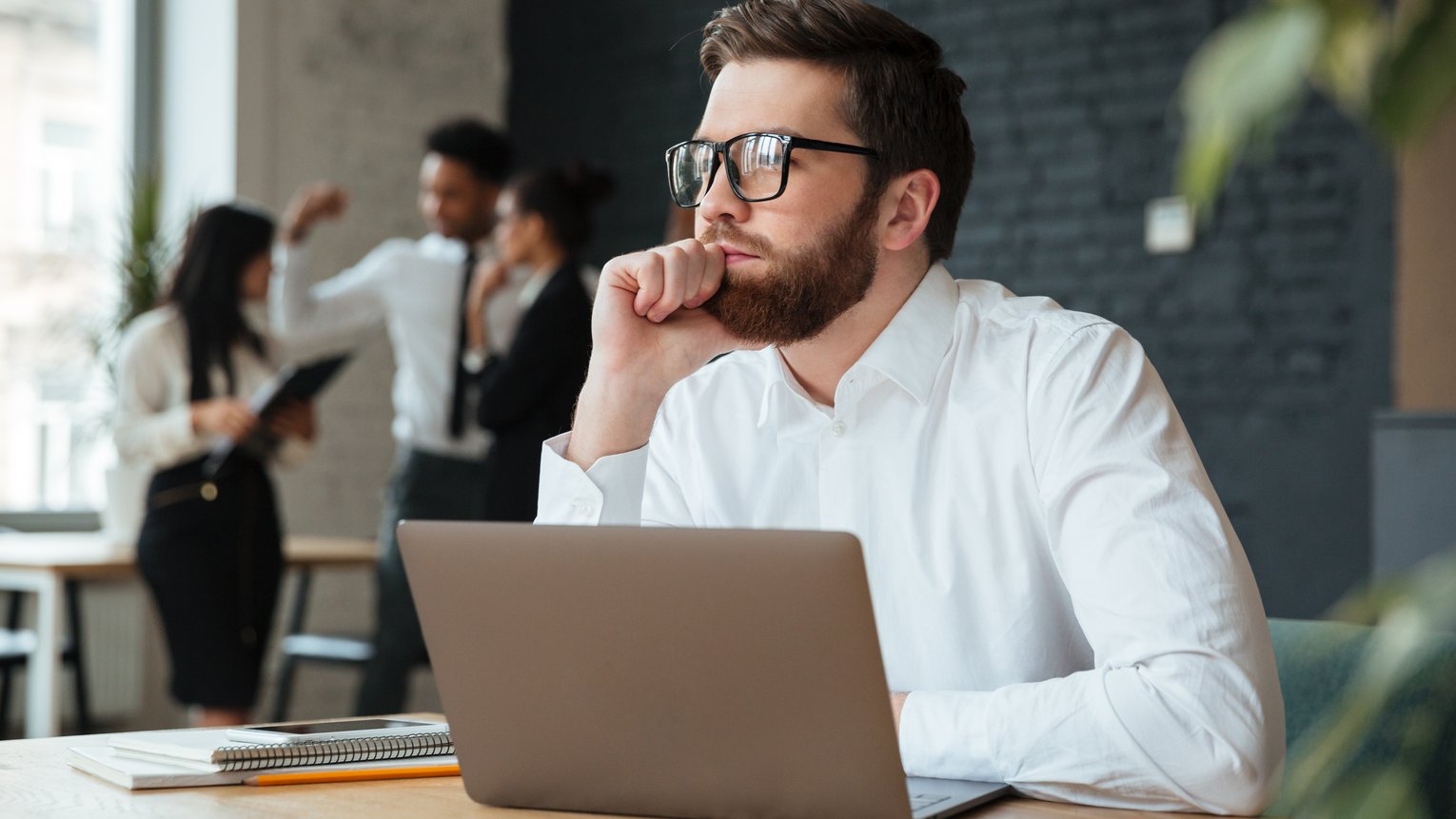 Mann sitzt grübelnd auf Laptop und schaut in die Ferne