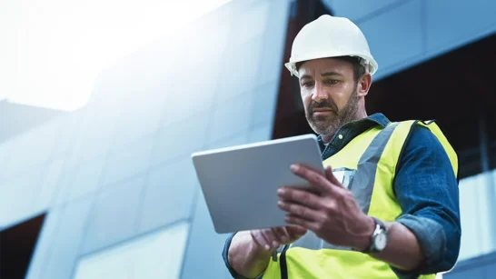 Man looks at tablet on construction site and is happy about the information he receives on the go thanks to digitalisation
