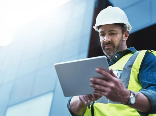 Mann blickt am Bau auf Tablet und freut sich über die Informationen, welche ihr durch die Digitalisierung auch Unterwegs erhält