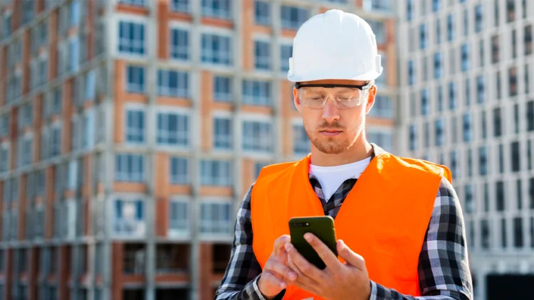 Bauarbeiter steht auf Baustelle und hat ein Handy in der Hand